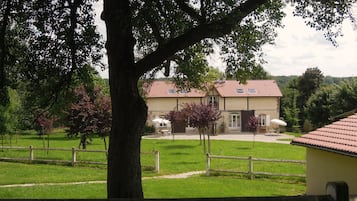 Une maison avec un toit recouvert de tuiles rouges, entourée d’une cour clôturée, agrémentée d’arbres et d’un chemin de gravier.