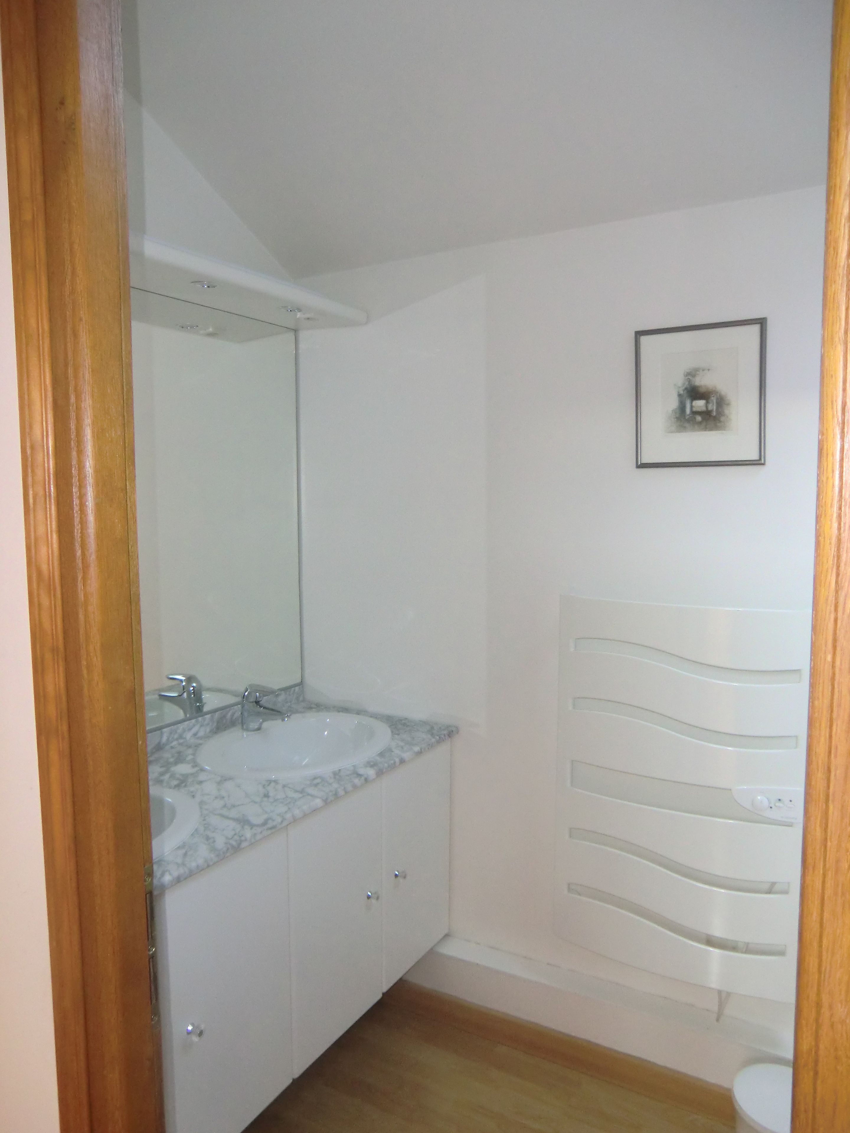 A bathroom with a white sink, mirror, and a framed picture on the wall.
