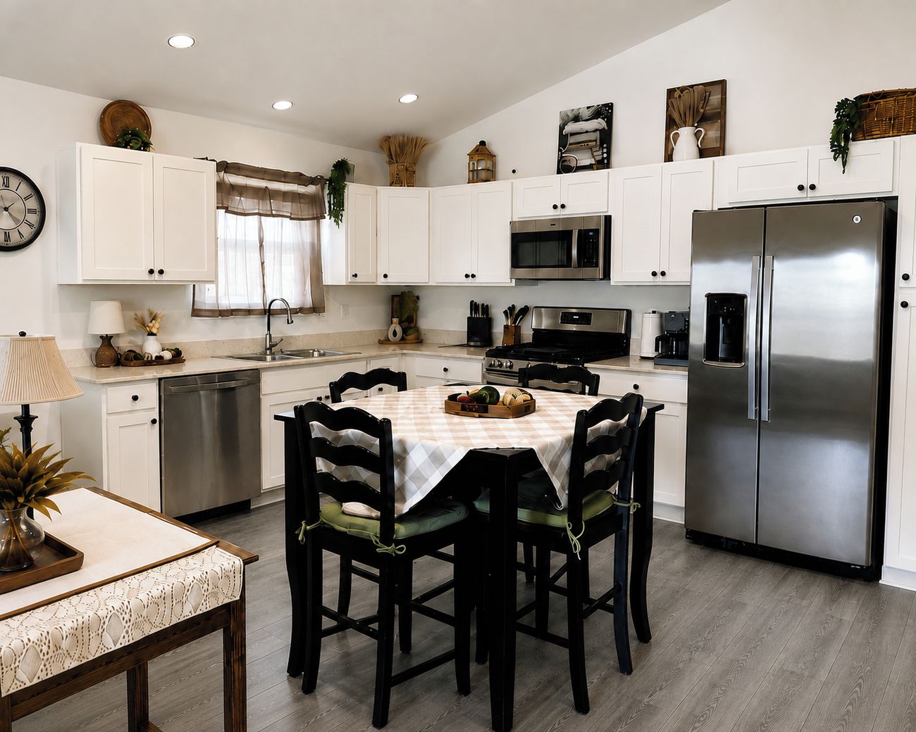 Una cocina moderna con armarios blancos, electrodomésticos de acero inoxidable, una mesa de comedor con sillas y un reloj en la pared.