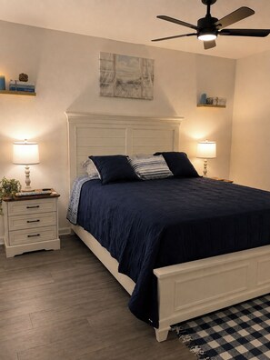 Une chambre à coucher comprenant un lit, des tables de chevet, un ventilateur de plafond et une œuvre d’art accrochée au mur.