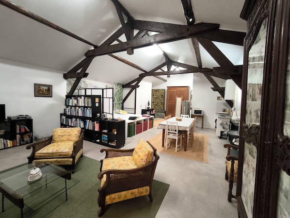 A spacious living room with high ceilings, exposed beams, a dining area, and a kitchen.
