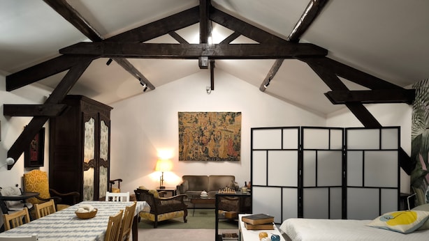 Um quarto acolhedor com uma mesa de jantar, cadeiras, um sofá, uma estante e um abajur decorativo.