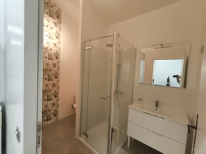 Een badkamer met een douchecabine van glas, een witte wastafel en een spiegel erboven.
