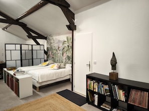 Een slaapkamer met een bed, een boekenkast, een bureau en een tropische muurschildering.