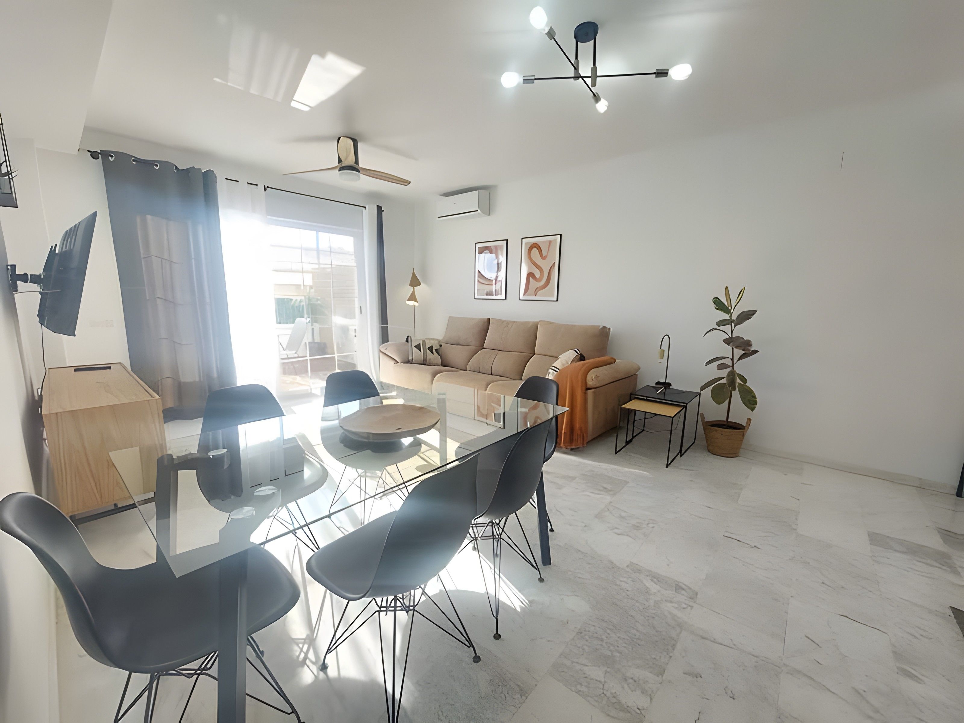 Una sala de estar moderna con una mesa de comedor de vidrio, sillas negras, un sofá color beige y una planta en maceta.