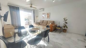 Una sala de estar moderna con una mesa de comedor de vidrio, sillas negras, un sofá color beige y una planta en maceta.