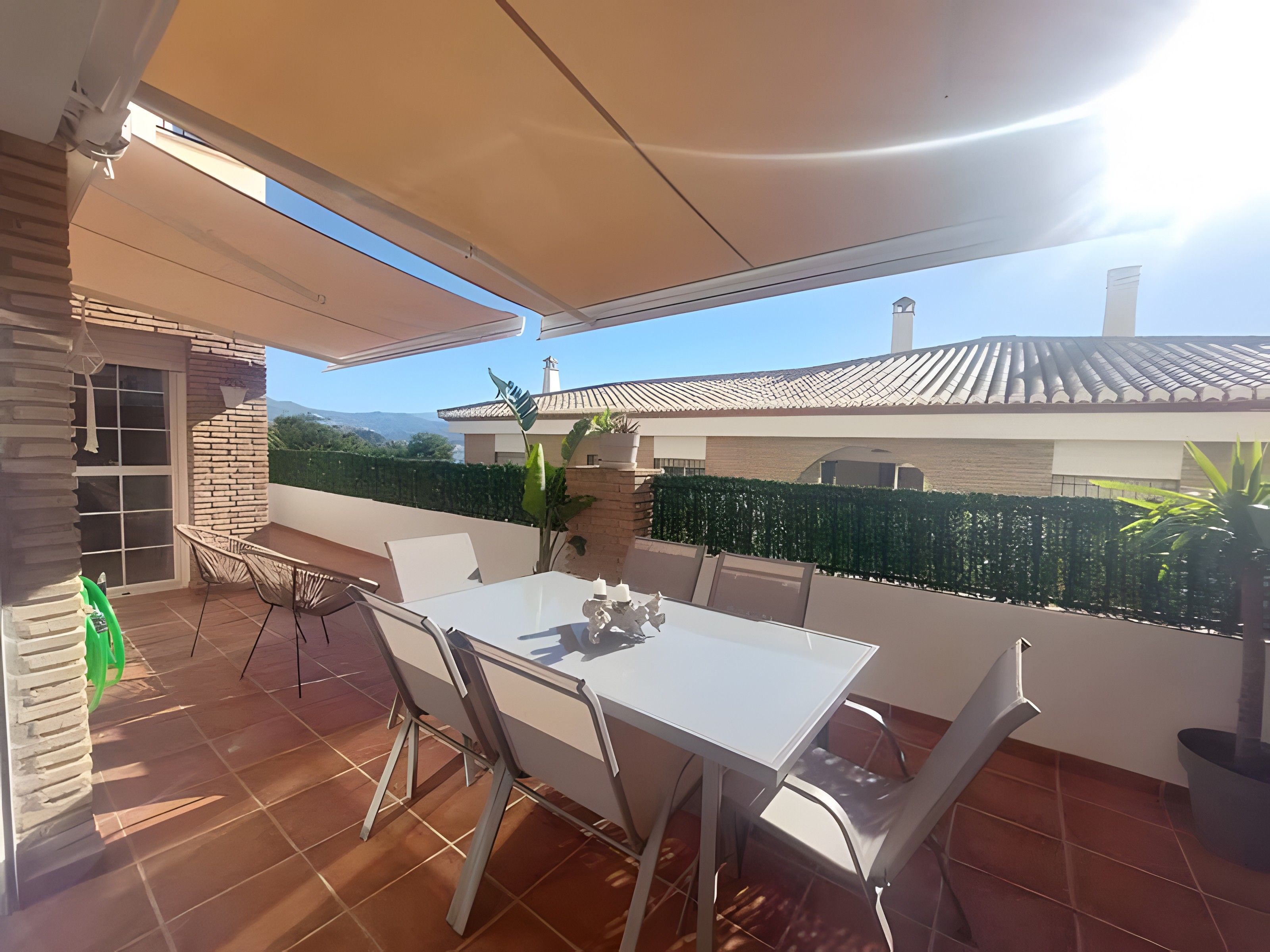 Eine Terrasse im Freien mit Tisch und Stühlen, einer Ziegelwand und Blick auf ein Haus und Berge.