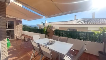 Eine Terrasse im Freien mit Tisch und Stühlen, einer Ziegelwand und Blick auf ein Haus und Berge.