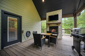 A covered outdoor patio with a stone fireplace, a grill, and a table with chairs. - 1BR Secluded Hot Tub Retreat (Broken Bow)