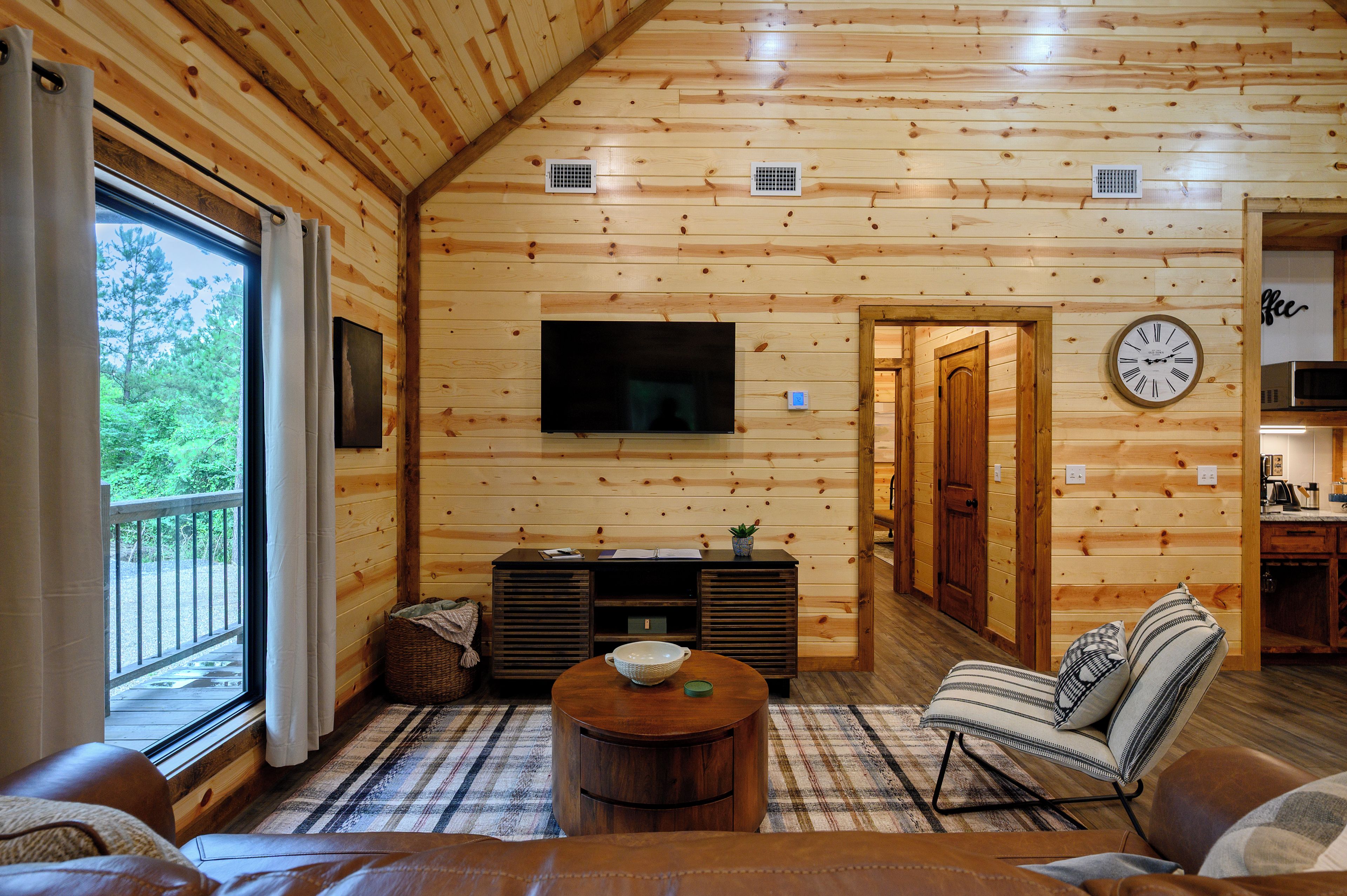 L’intérieur d’un chalet en bois comprend un salon, un téléviseur, une horloge et une vue sur l’extérieur.