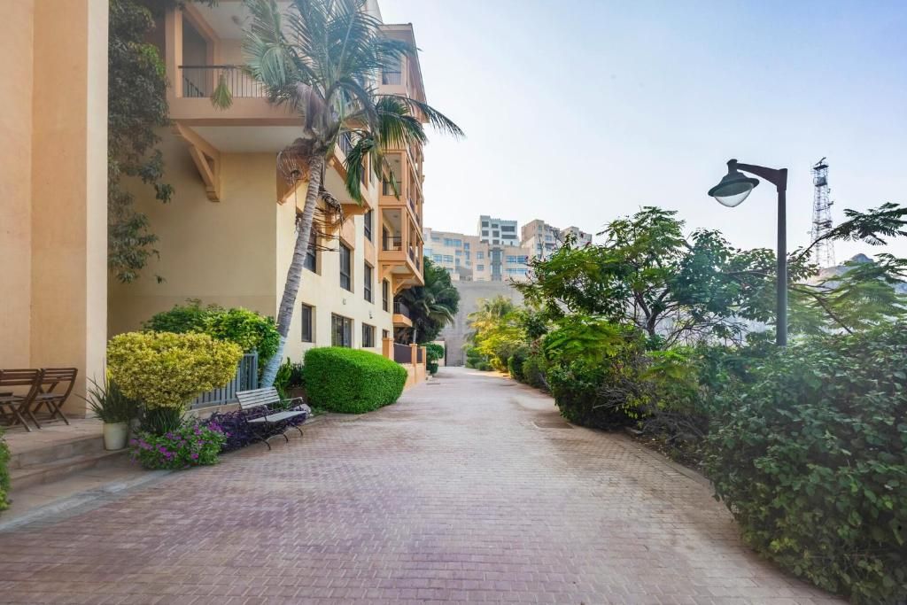 Un sendero pavimentado bordeado por follaje y un edificio con balcones.