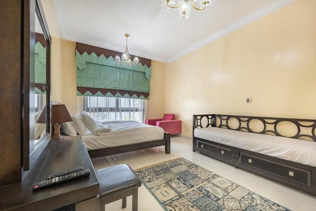 A bedroom with a bed, a desk, a chair, a small table, a rug, and a window with curtains.