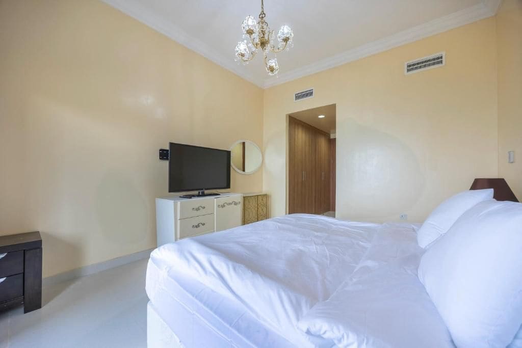 Une chambre d’hôtel avec un lit, une télévision, une commode et un lustre.