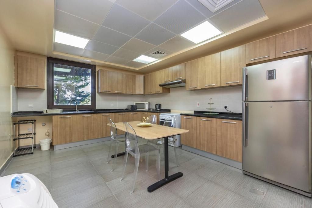 A modern kitchen with wooden cabinets, a stainless steel refrigerator, and a dining area with a table and chairs.