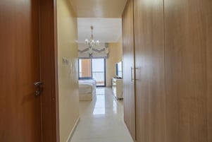 A hallway leading to a bedroom with a bed, a desk, and a wardrobe.