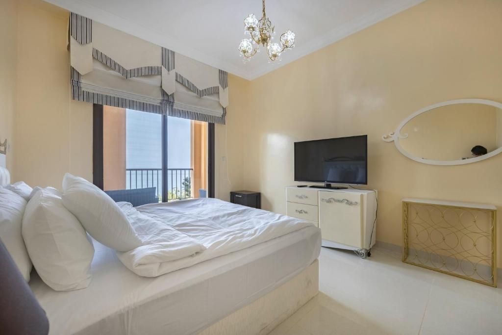 A bedroom with a bed, a television, a dresser, and a window with curtains.