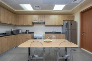 A modern kitchen with wooden cabinets, a stainless steel refrigerator, a microwave, and a dining table with clear chairs.