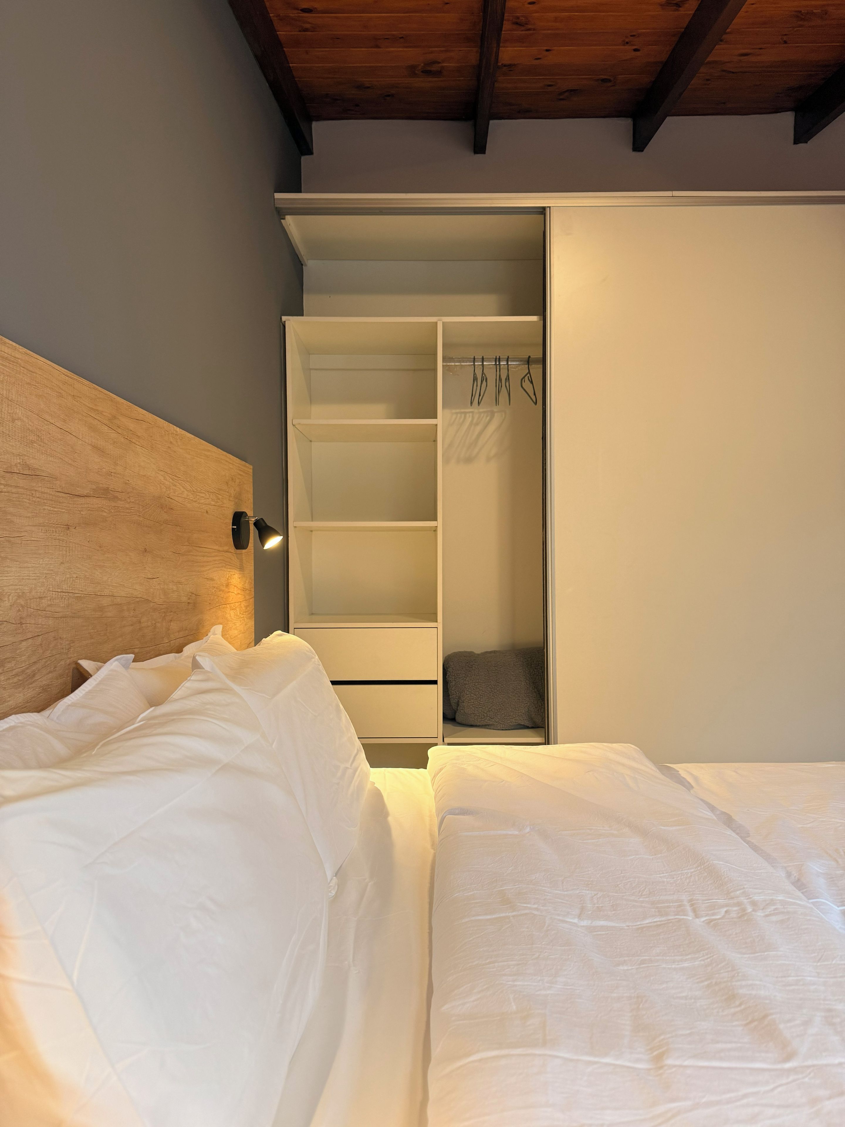 A bedroom with a wooden headboard, a bed with white bedding, and a built-in wardrobe with hanging space.