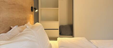 A bedroom with a wooden headboard, a bed with white bedding, and a built-in wardrobe with hanging space.