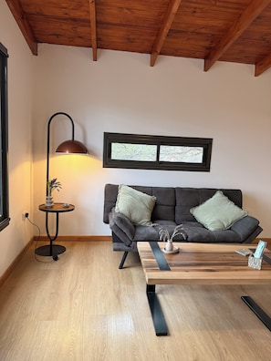 A cozy living room with a dark grey sofa, two green pillows, a round side table with a lamp, and a wooden coffee table. - Stanza II. Lovely 1-bedroom apartment with AC in enchanting Córdoba (Córdoba)