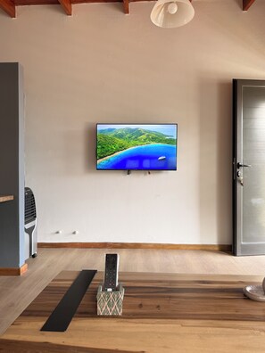 A room with a television mounted on the wall displaying a scenic landscape, a remote control on a wooden surface, and a door to the right.