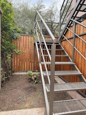 A metal staircase leading to a wooden deck with a wooden fence in the background.