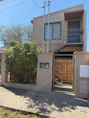 A modern two-story building with a gated entrance, a staircase, and a small outdoor area with a tree.