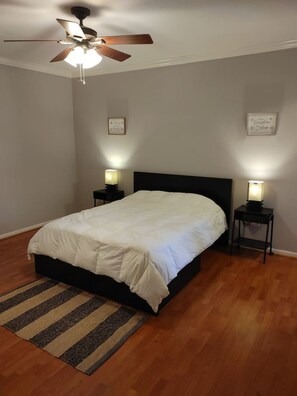 A bedroom with a bed, a ceiling fan, two bedside tables with lamps, a rug, and a wall with two framed pictures. - Med Center Condo With Pool Gym and Balcony (Houston)