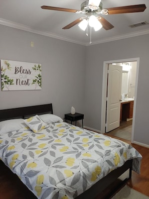 A bedroom with a bed, a ceiling fan, a nightstand, and a door leading to a bathroom. - Med Center Condo With Pool Gym and Balcony (Houston)