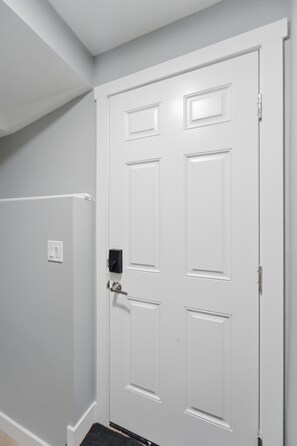 A white door with a handle and a keyhole, a doorknob, and a small light switch on the wall. - Mountain Escape Deluxe King Suite (Free Parking) (Cochrane)
