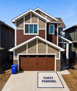A two-story house with a brown garage door and a 'Guest Parking' sign in front. - Mountain Escape Deluxe King Suite (Free Parking) (Cochrane)
