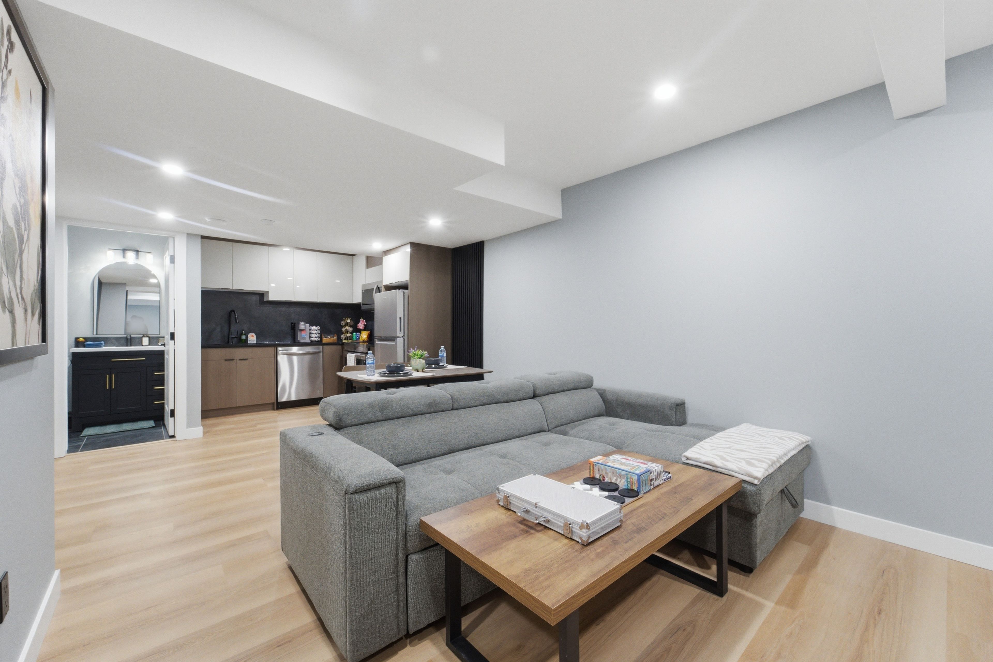 Un espace de vie moderne avec un canapé d’angle gris, une table basse en bois et une cuisine en arrière-plan.