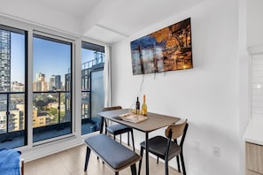 Een eetgedeelte met een tafel, stoelen en een bank. Een groot raam biedt uitzicht over de stad.