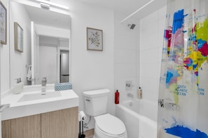 Een moderne badkamer met een wit wastafel, toilet en bad. Er hangt een lijst met bloemkunst aan de muur en het douchegordijn is versierd met een wereldkaart.