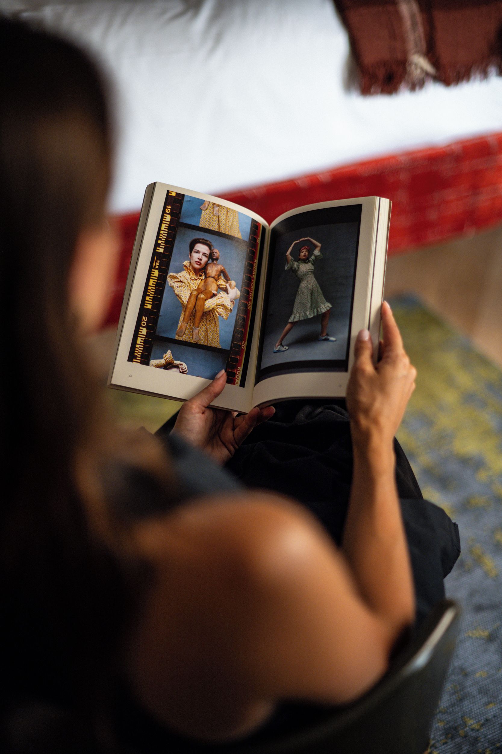 Une personne assise sur un lit, en train de lire un livre contenant des photographies.