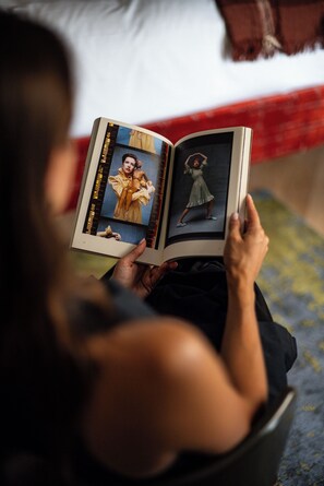 A person sitting on a bed, reading a book with photographs. - The House of Delray (Tel Aviv)