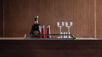 Un coin bar avec une bouteille de Hennessy XO, deux verres rouges et deux verres transparents disposés sur un plateau.