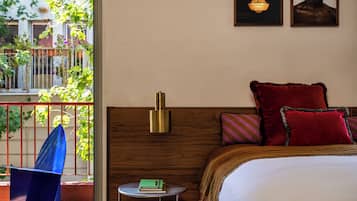 Une chambre à coucher avec une tête de lit en bois, une table de chevet ronde sur laquelle repose un livre vert, et un oreiller rouge.