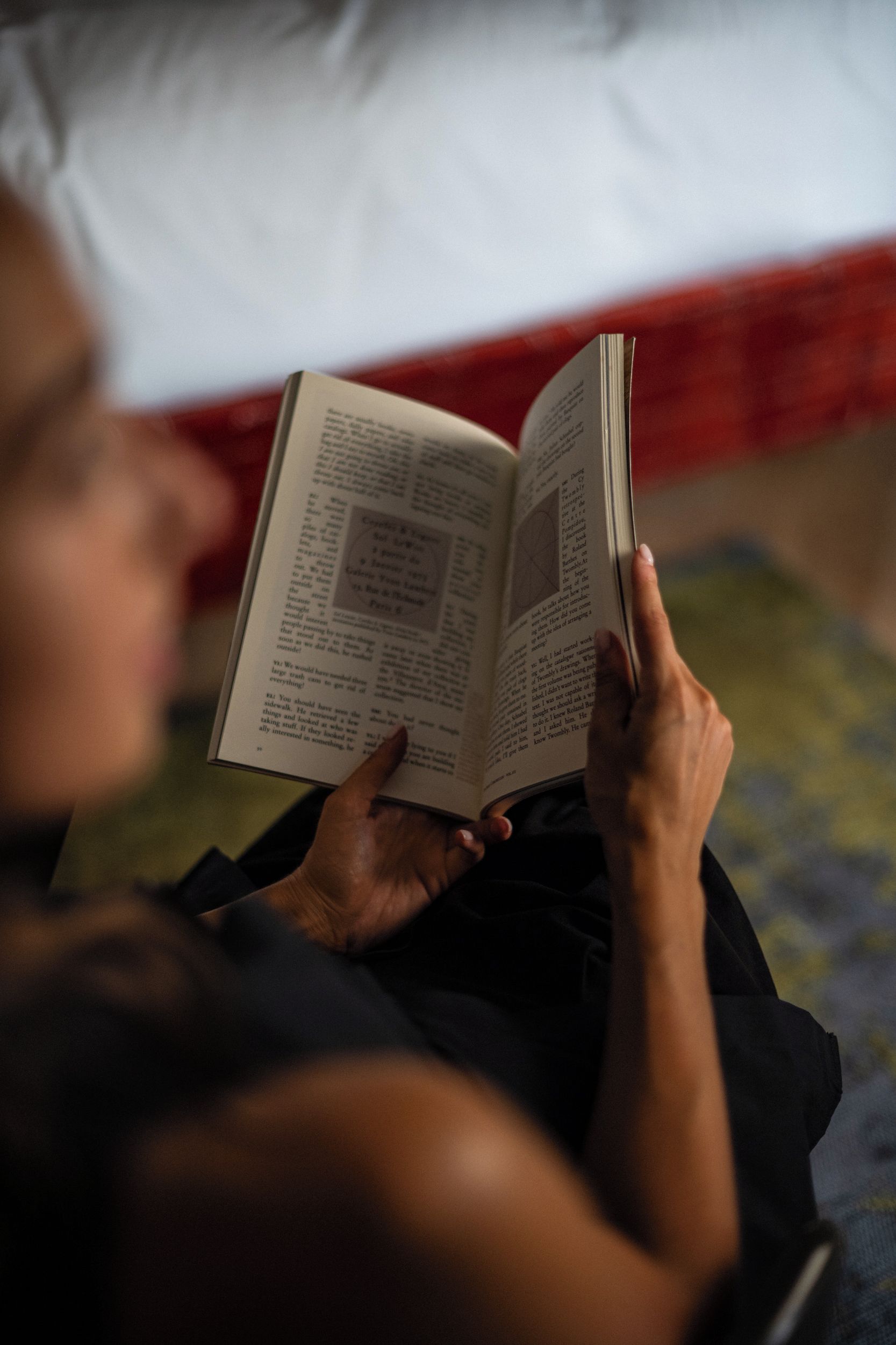 A person reading a book in a room with a bed and a blanket.