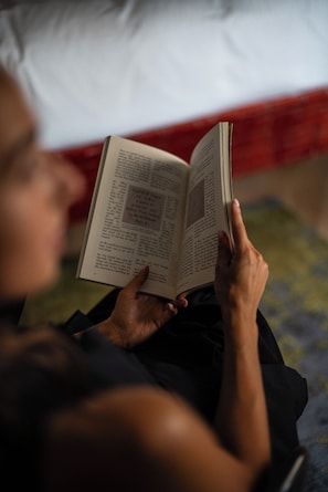 Una persona leyendo un libro en una habitación con cama y manta.