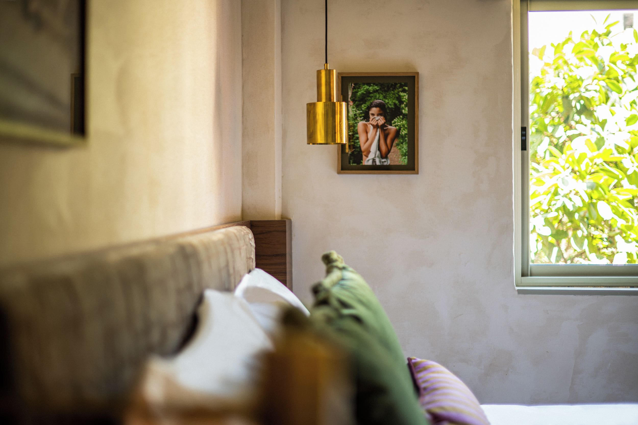 Una stanza con un letto, un lampadario, un quadro appeso al muro e una finestra che dà su del verde.