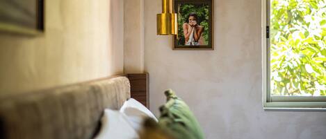 Una stanza con un letto, un lampadario, un quadro appeso al muro e una finestra che dà su del verde.