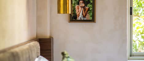 A bedroom with a bed, a hanging light fixture, a framed picture on the wall, and a window with a view of greenery.