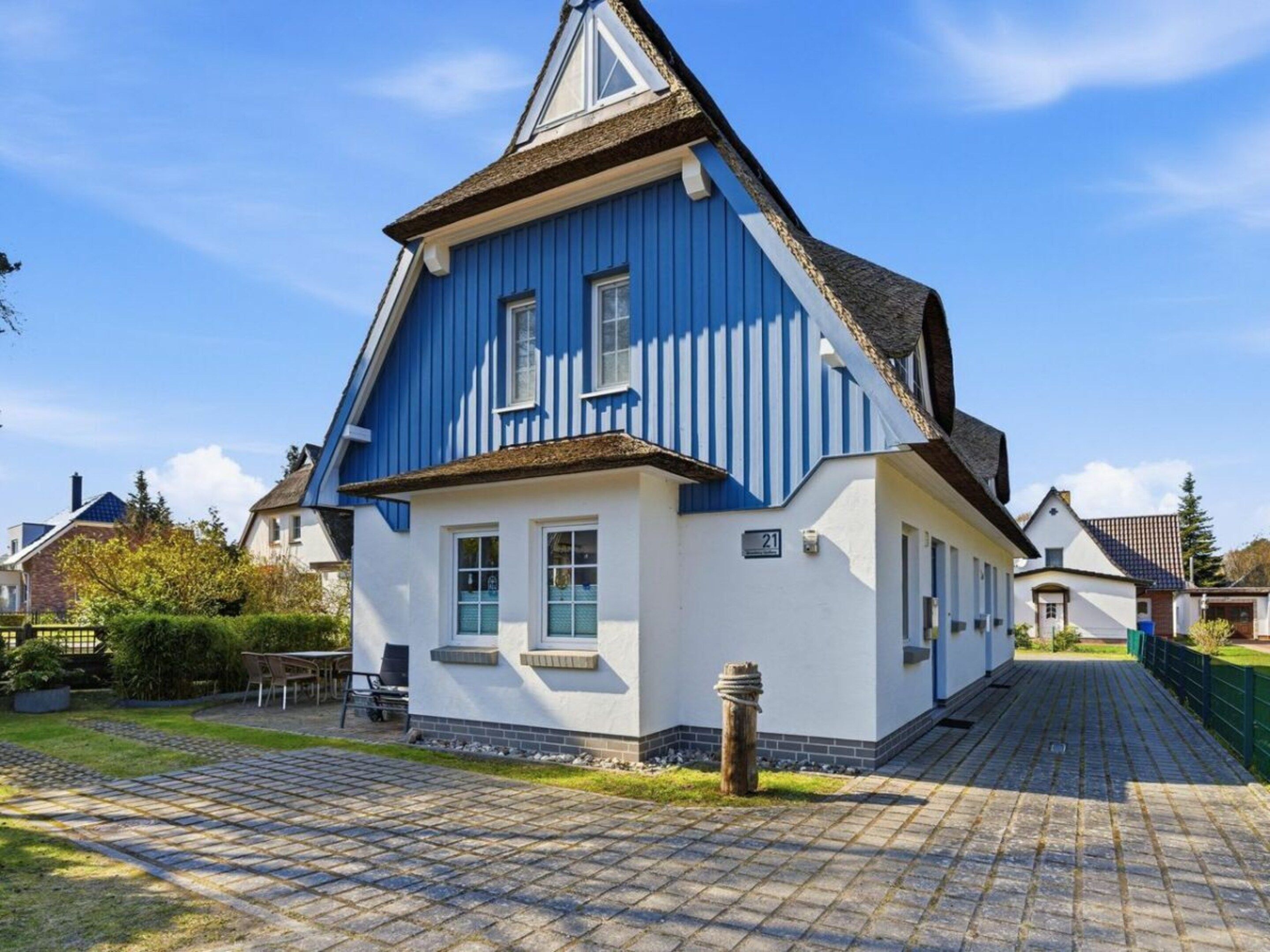 Ein zweistöckiges Haus mit blauer Fassade und weißer Verzierung, einer gepflasterten Auffahrt und einem kleinen Garten.