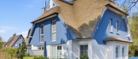 A traditional house with a steeply pitched roof, a visible chimney, and a well-maintained garden.