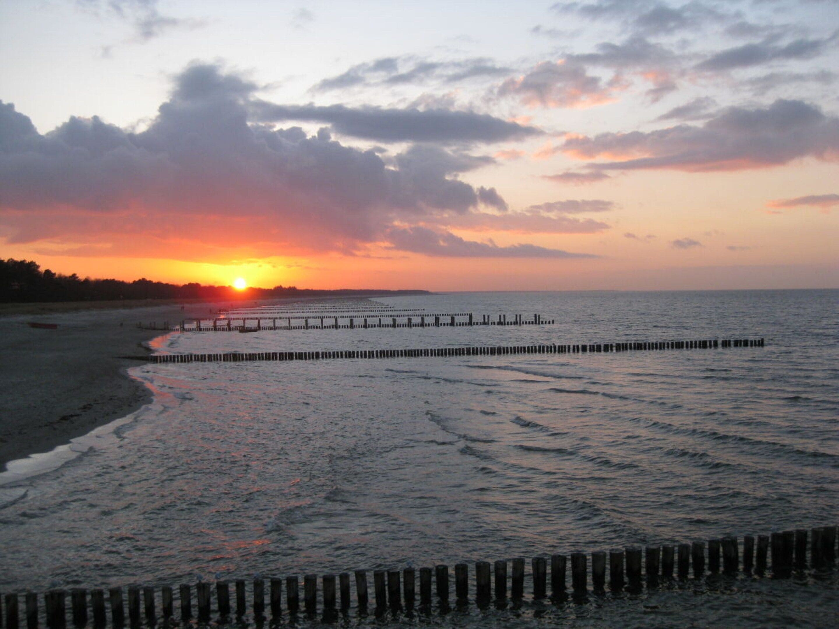 A beach with a wooden pier extending into the water during sunset.