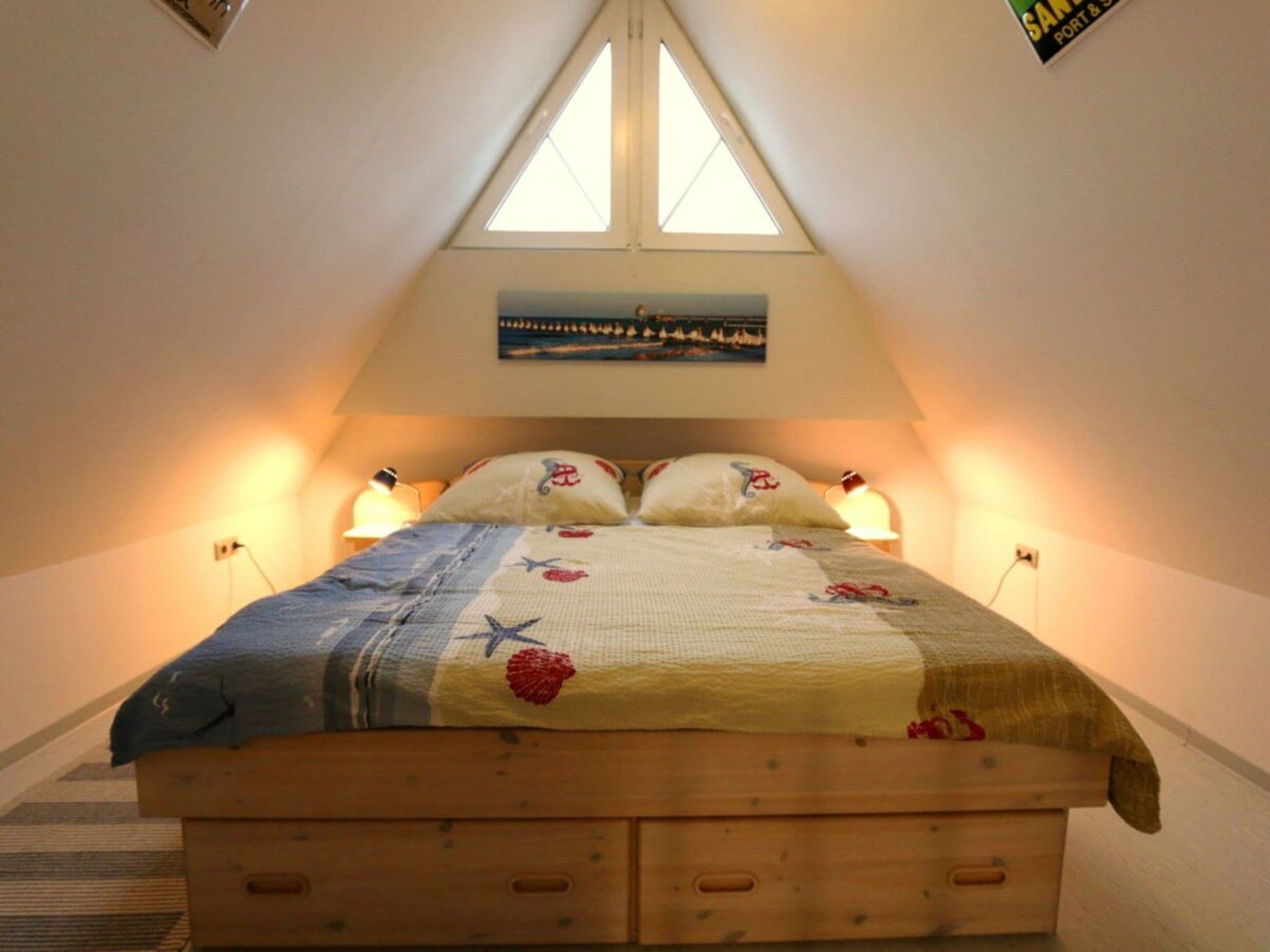 A bedroom with a sloped ceiling, a bed with a floral bedspread, two bedside lamps, and a painting above the bed.