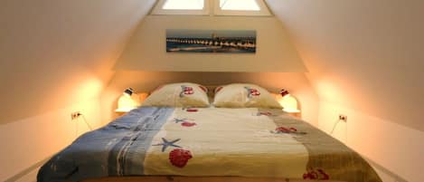 A bedroom with a sloped ceiling, a bed with a floral bedspread, two bedside lamps, and a painting above the bed.