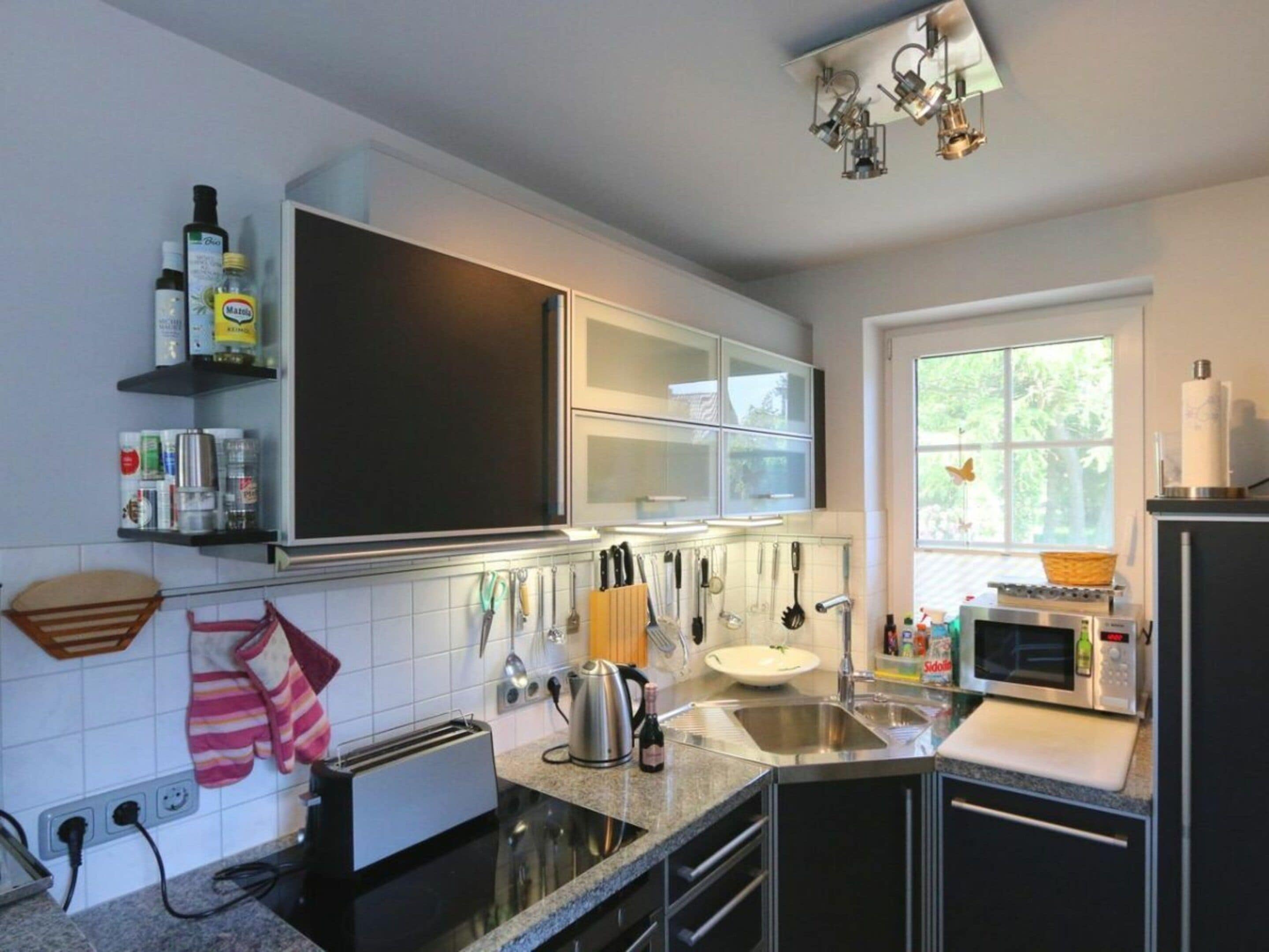 A modern kitchen with a microwave, toaster, and sink. There are cabinets above the counter and a window with a view of greenery.
