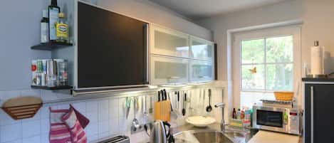 Cocina moderna con microondas, tostadora y lavamanos. Hay armarios sobre la encimera y una ventana con vistas a la vegetación.